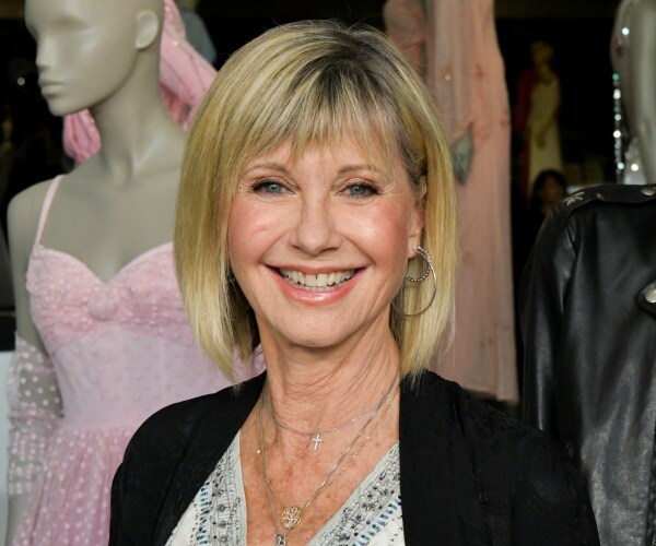 newton-john in a white top and black cardigan with a mannequin wearing a pink dress behind her