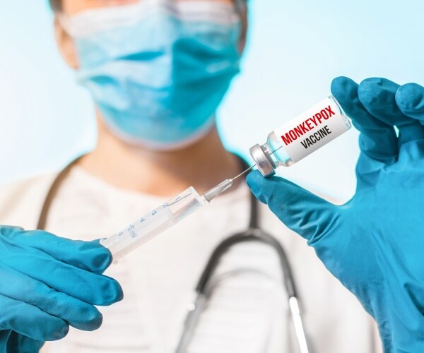 healthcare worker with mask/gloves holding syringe labeled 'monkeypox vaccine'