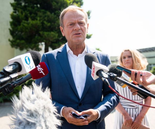 tusk in a navy blue suit and white shirt with many microphones pointed toward him