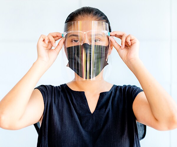 a brunette woman dons a face shield and a face mask