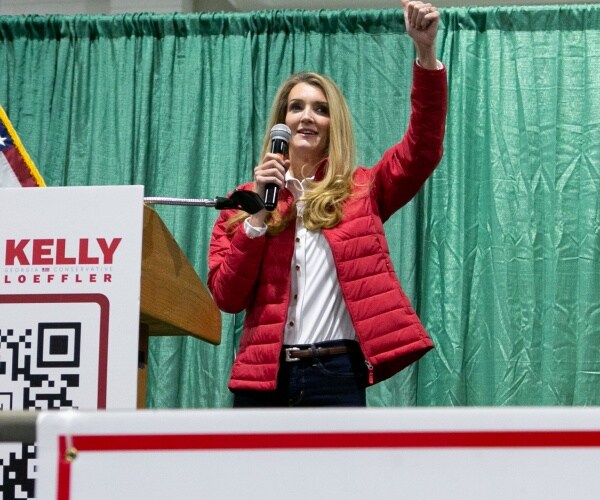 kelly loeffler stands next to a qr code behind a sign of support