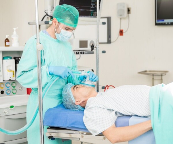 male anesthesiologist administers sedative with face mask to patient in operating room