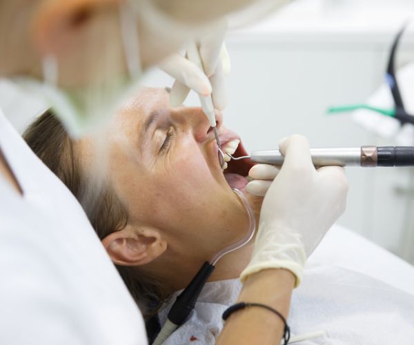 patient in dentists chair getting teeth cleaned by hygienist 