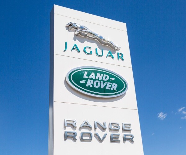 Jaguar and Land Rover logo sign against blue sky.