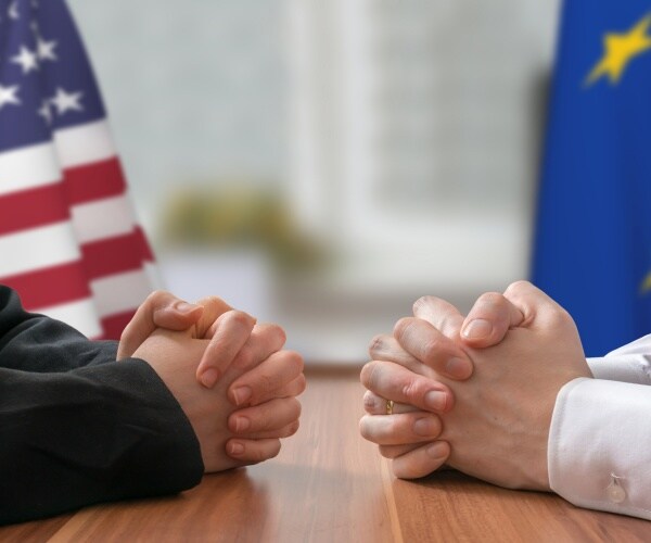 politicians sitting at a table with the us and eu flags near them