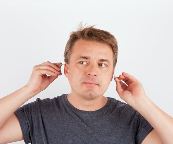 man in t-shirt holds hearing aids near his ears