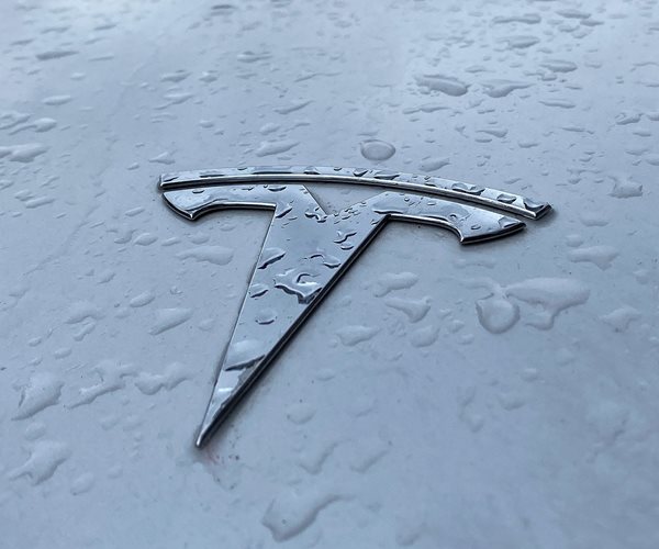 the stylized t logo of tesla is seen close up on the hood of a vehicle