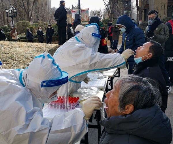 people are having their throats swabbed in line by people in hazmat suits