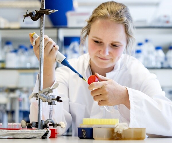 woman in a white labcoat uses a pipette while working in a lab