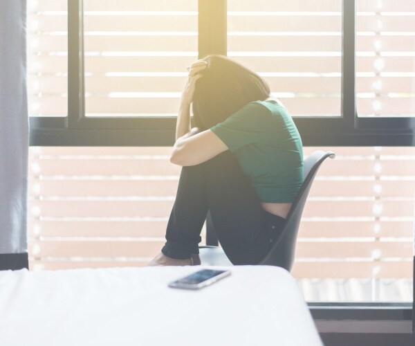 woman sitting in chair by window in despair, cell phone on counter near her
