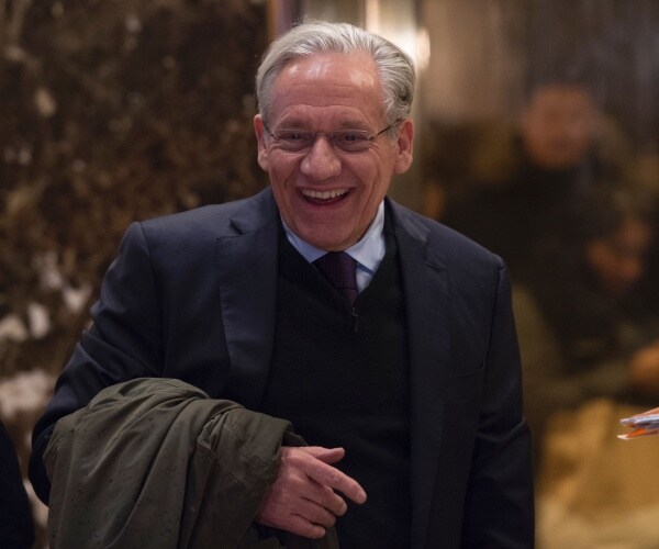 woodward in a navy blue suit and vest with a light blue shirt and tie holding a green jacket