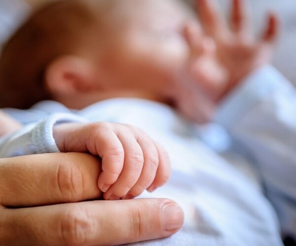 adult's hand holding an infant's hand
