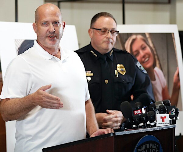 Joe Petito speaks to the media, with a police officer and a large poster of his missing daughter over his left shoulder