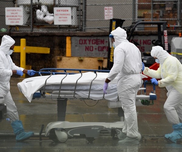 people in ppe gowns and masks roll a gurney through an outdoor parking log