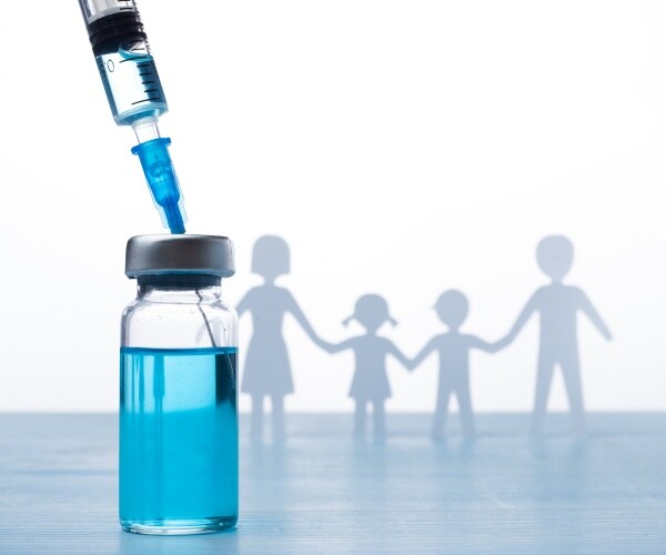 vial with flu vaccine, syringe, paper cut out of family of 4 in background