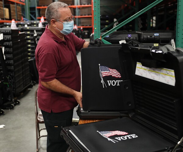 a worker wearing a mask prepares a voting booth for use in the election
