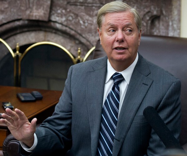 lindsey graham is seated and gestures as he answers reporter's questions