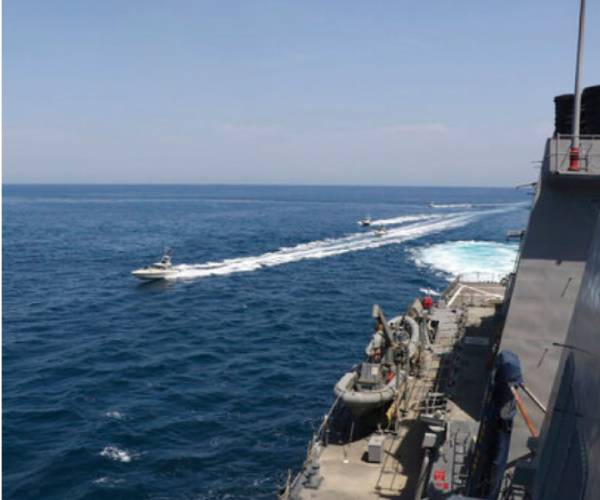 a small boat speeds past a military ship
