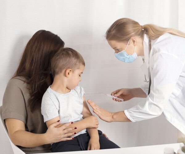 mom holding young boy, healthcare practitioner with syringe
