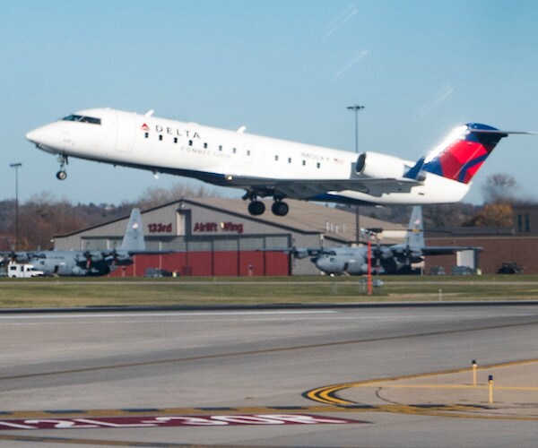 a delta airlines jet takes off before a pale blue sky