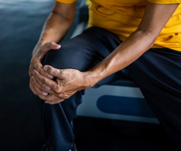 man wearing a yellow shirt and black pants holding his knee in pain
