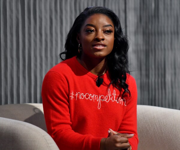 gymnast simone biles sits on a chair wearing a red shirt