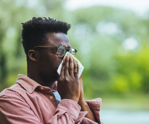man outside blowing nose