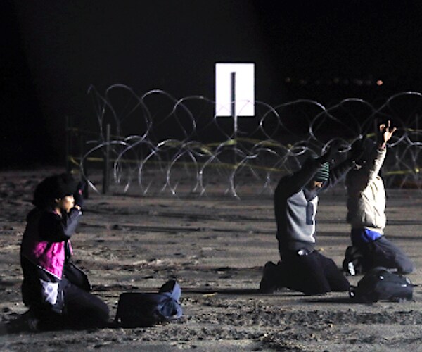 migrants are on their knees with their arms up while being arrested for trying to illegally cross the border