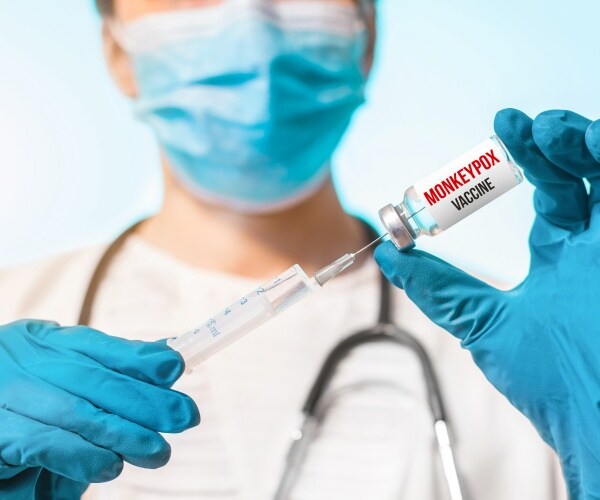 healthcare worker with protective clothing holding a syringe, monkeypox vaccine vial