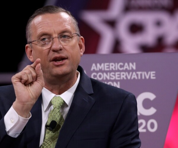 collins in a black suit and light green tie speaking at cpac