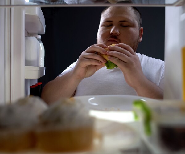 an overweight man eating out of the refrigerator