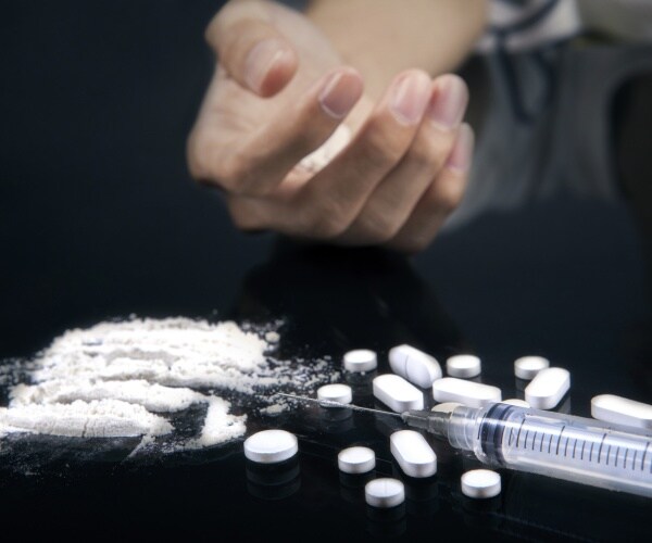 drug overdose is depicted with a hand stretched out near pills, powder, and a syringe