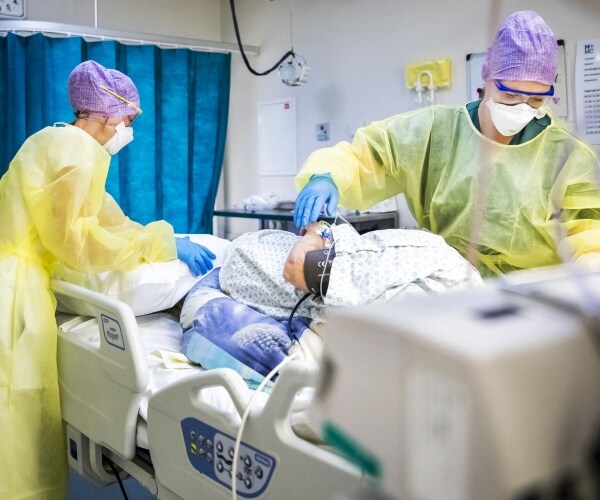 nurses in yellow protective suits and purple caps take care of a patient