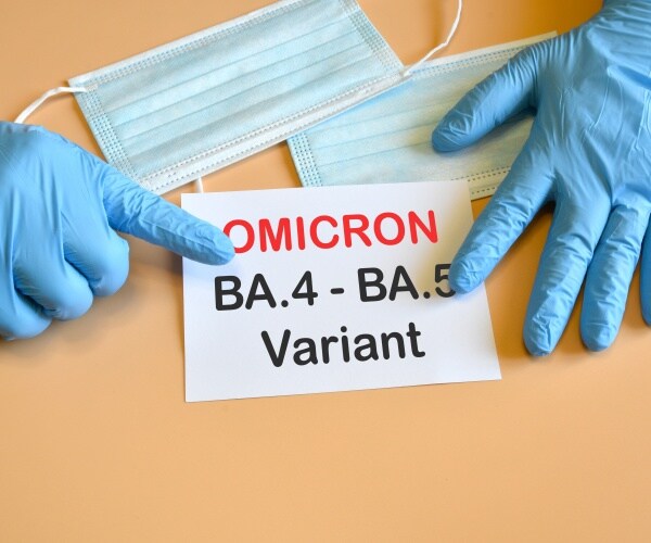 surgical-gloved hands pointing to a square piece of paper saying 'omicron BA.4 BA.5'
