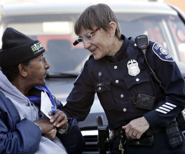 a uniformed police woman, wearing a video camera on her eyeglasses, on right, talks with a man 