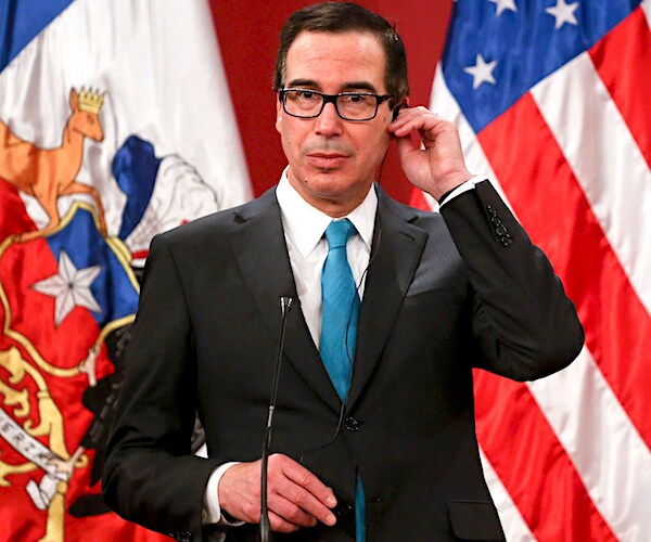 steven mnuchin adjusts his ear piece while preparing for a news conference with an american flag in the background