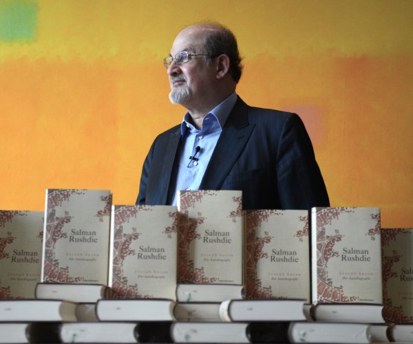 author salman rushdie poses behind stacks of his books