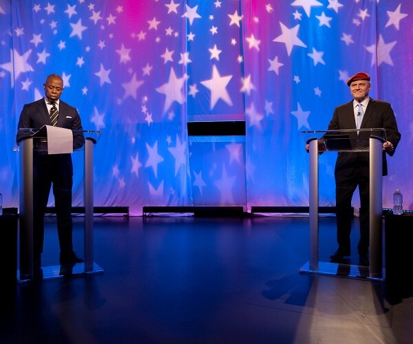 eric adams and curtis sliwa stand behind podiums before debate