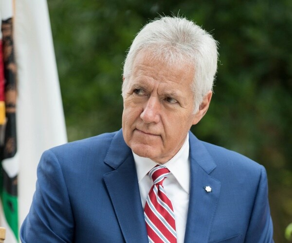 trebek in a blue blazer and red and white striped tie sitting outside