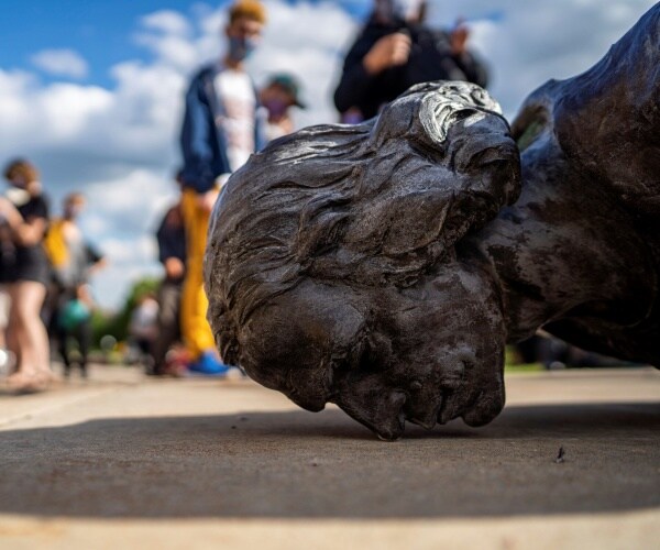 columbus statue fallen face to the ground while a crowd stands nearby