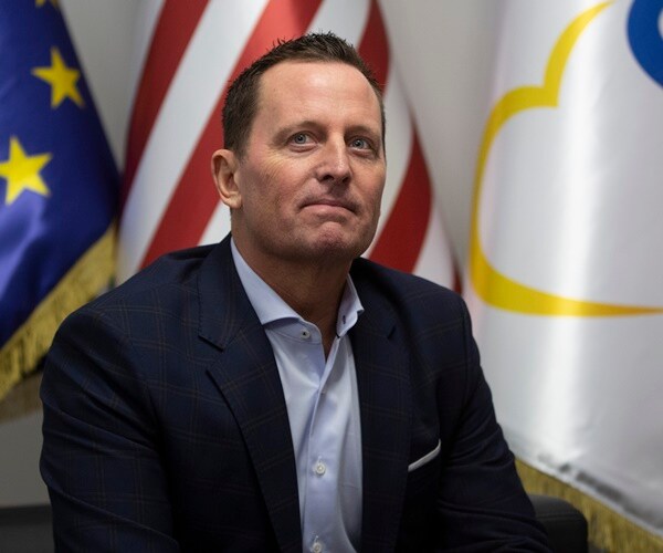 rick grenell sits in front of flags