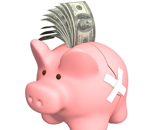 pink piggy bank with white medical tape over crack and stack of dollars sticking out on top