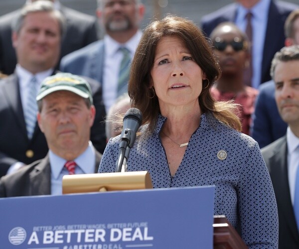 cheri bustos stands at a podium in front of other democratic officials