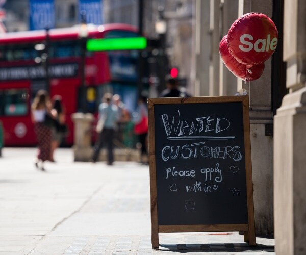 a sign says "customers please apply within" outside of a store with sale balloons