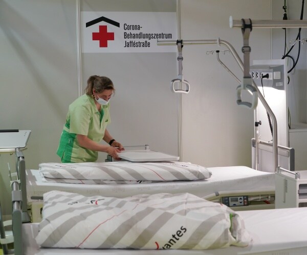 nurse in green scrubs and face mask prepares beds in a german hospital