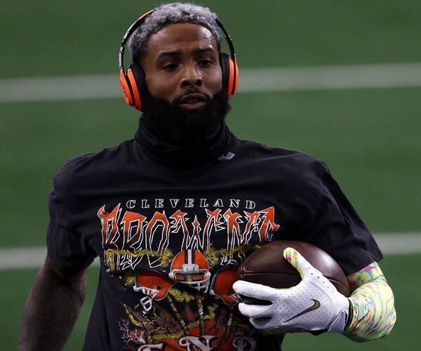 odell beckam carries a football, wearing headphones and gloves