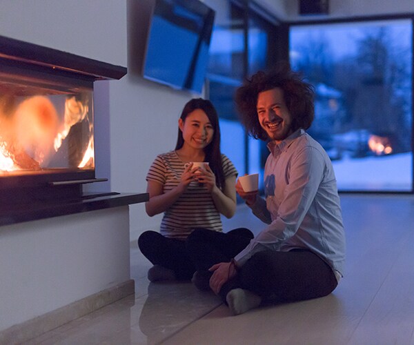 a man and woman drinking coffee by a fireplace
