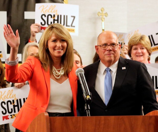 shulz waving with hogan standing beside her and supporters with political signs behind her