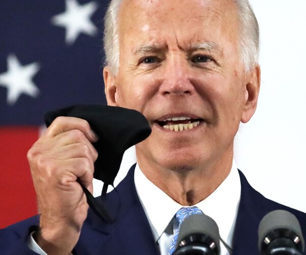 joe biden speaks on stage while holding up a face mask
