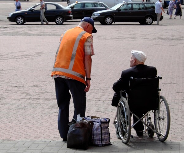 man in wheelchair in Ukraine train station with bags and train worker talking to him